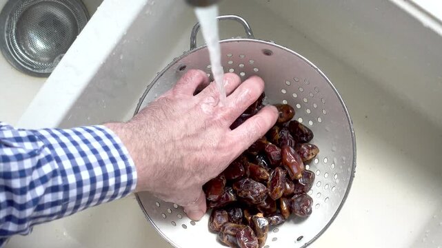 Male hands wash dried dates in a mesh strainer under running water in a kitchen sink. Concept of healthy eating and using natural sweeteners. Top view. Ideal for nutrition, vegan diet, cooking content