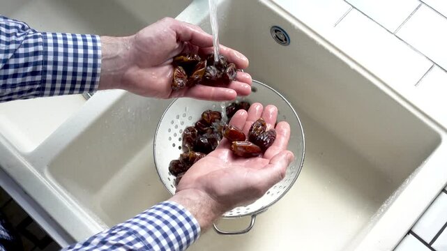 Male hands wash dried dates in a mesh strainer under running water in a kitchen sink. Concept of healthy eating and using natural sweeteners. Top view. Ideal for nutrition, vegan diet, cooking content