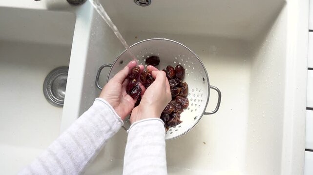 Female hands wash dried dates in a mesh strainer under running water in a kitchen sink. Concept of healthy eating and using natural sweeteners. Ideal for nutrition, vegan diet, and cooking content