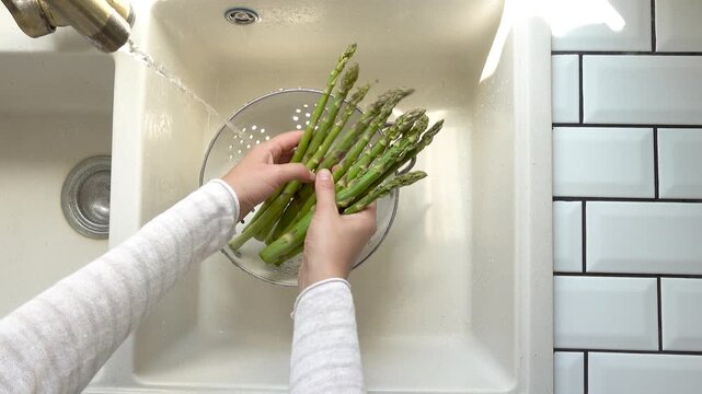 Female hands wash asparagus under running water over a metal colander in a kitchen sink. Concept of healthy eating and using natural sweeteners. Ideal for nutrition, vegan diet, and cooking content