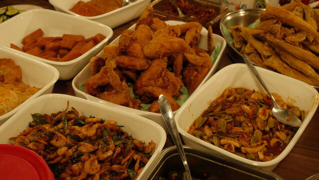 Traditional Malay nasi lemak spread with fried chicken wings, crispy fish, petai and sambal dishes on table close up