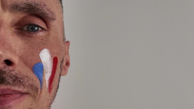 A close-up of a man painting his cheek in the colors of the French flag. A patriotic fan preparing for a national team match