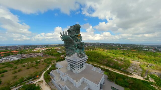 Cinematic FPV drone shot of Garuda Wisnu Kencana statue in Bali, Indonesia with panoramic cityscape and ocean horizon. Iconic landmark of Balinese culture and Hindu mythology.