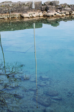 Eau turquoise et limpide d'un lac avec reflets de la digue en pierre , d'un m&acirc;t et fonds visibles
