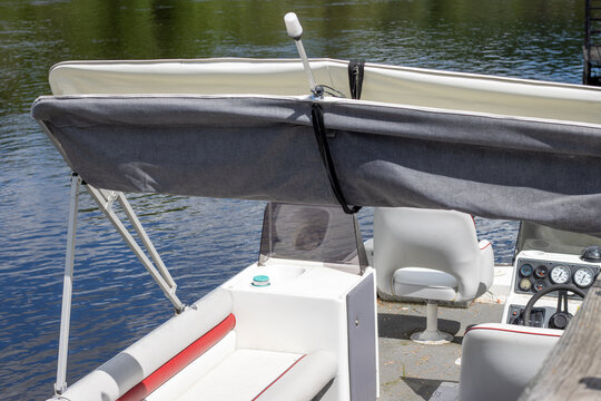 Close up view of the helm and seating area of a pontoon boat docked on a calm river.