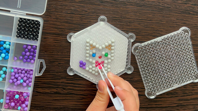 Hands place colorful fuse beads on hex boards. Ideal for DIY craft ads, hobby blogs, kids activity banners.
