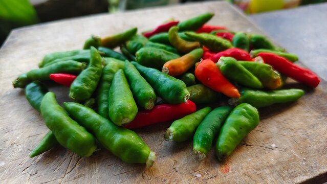 A pile of fresh raw green cayenne peppers or 'cabai rawit' on a traditional wooden cutting board, spicy Indonesian cooking ingredients