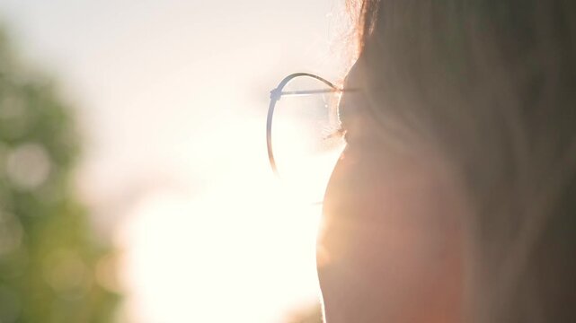 Portrait of young woman wearing glasses at sunset against natural backdrop in park. Concepts for connection with nature, outdoor walks, mental health, and harmony with the environment.