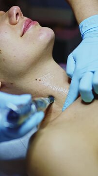A person receives a beauty treatment in a salon. Their neck is the focus as a professional uses a device to apply products for skin care. The room shows signs of a beauty setting.