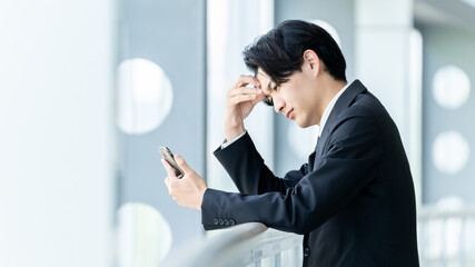 スマートフォンを見ながら悩む男性ビジネスマン, Businessman Looking Worried While Viewing a Smartphone © Trickster*