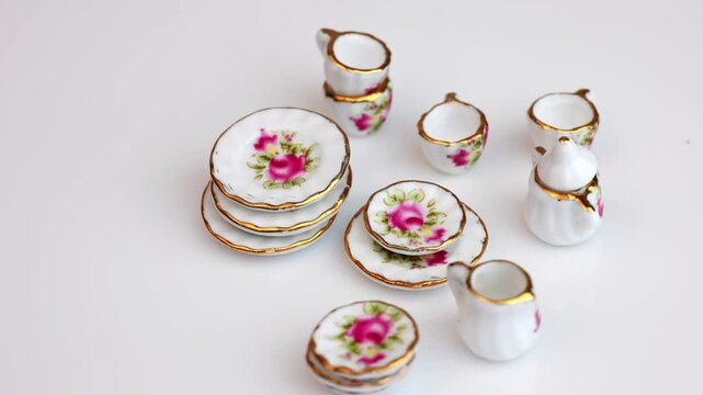 Miniature porcelain tea set with floral rose pattern rotating on white background, tiny dollhouse kitchenware collection.