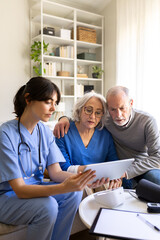 Obraz premium Nurse showing information on tablet to senior couple at home visit. Vertical image.
