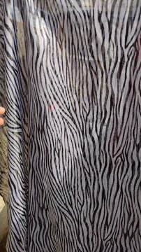 Close-up of a hand touching a translucent lightweight fabric with a black and white zebra stripe animal print pattern. Vertical video for commercial textile retail and fashion design ads.