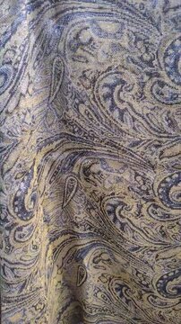Close-up of a heavy jacquard fabric with an intricate golden paisley pattern and metallic threads gently swaying. Vertical video for commercial textile retail, luxury apparel, and decor ads.