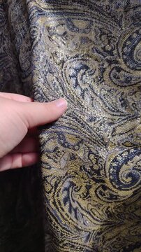 Close-up of a hand touching a heavy jacquard fabric with an intricate golden paisley pattern and metallic threads. Vertical video for commercial textile retail, luxury apparel, and decor ads.