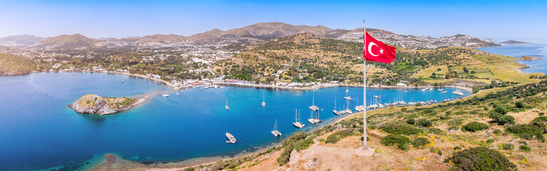 Naklejka premium Bodrum Gumusluk bay panorama with a Turkish flag and many sailboats in the Aegean Sea on a sunny day