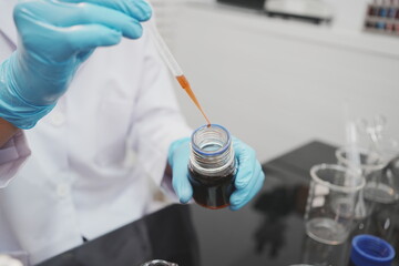 Fototapeta premium Close-up of a lab worker in blue gloves using a pipette to transfer brown liquid from a bottle in a clean laboratory setting.