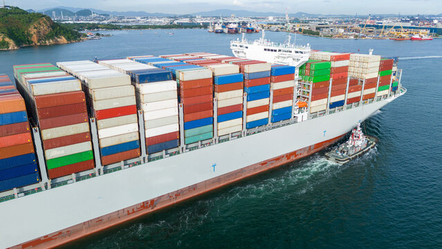 stern cargo container ship shipping containers approaching a bustling commercial port, representing global maritime logistics, international trade, and import export.