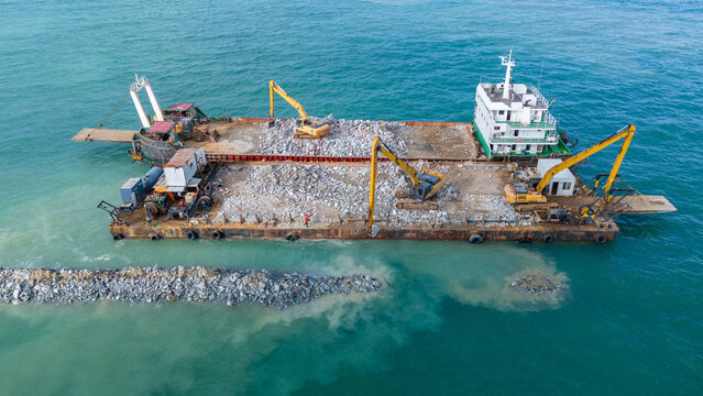 large construction barge equipped with excavators performing coastal land reclamation and rock armor installation at sea, representing maritime engineering, infrastructure development,