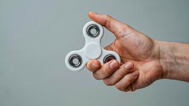 Hand holding fidget spinner isolated on gray background for stress relief and focus concept