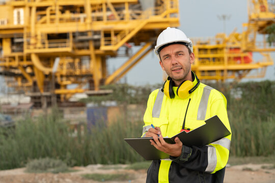 Industrial engineer holding a check list clipboard and walkie-talkie at an offshore energy platform. Concept of workplace safety compliance, power infrastructure, and professional engineering