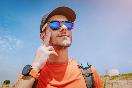 Man applying sunscreen to face outdoors under blue sky, protecting skin from harmful UV rays during summer activity