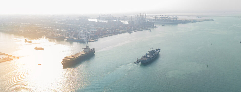 naval warship escorting a large commercial container ship near a busy industrial port, symbolizing maritime security, naval patrol, global trade protection, and geopolitical stability.