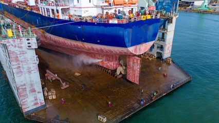 cargo ship's hull and propeller in a dry dock, undergoing high-pressure water cleaning and maintenance, highlighting maritime engineering and ship repair operations. © Yellow Boat