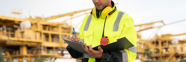 Industrial engineer holding a check list clipboard and walkie-talkie at an offshore energy...