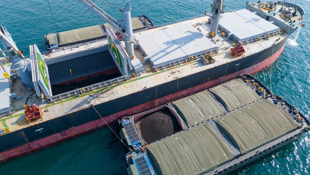 large bulk carrier ship transferring dark bulk cargo like coal or minerals into smaller barges alongside it in the open sea, representing maritime logistics and global supply chain.