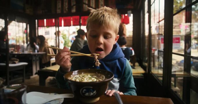 Child Eating Noodles with Chopsticks in Japanese Restaurant - Medium Shot
