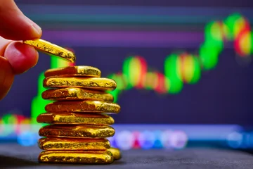 Close up investor hand stacking gold bullion bars with financial stock market graph background © I Viewfinder