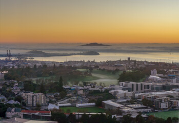 Obraz premium Auckland, New Zealand. Sunrise over the city skyline with fog rolling in from the harbor, casting a mystical glow on the port and surrounding buildings.