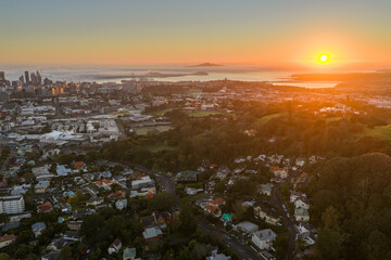 Fototapeta premium Sunrise over Auckland, New Zealand. The city skyline emerges from a layer of low clouds as the sun casts a warm glow over the harbor and surrounding hills.