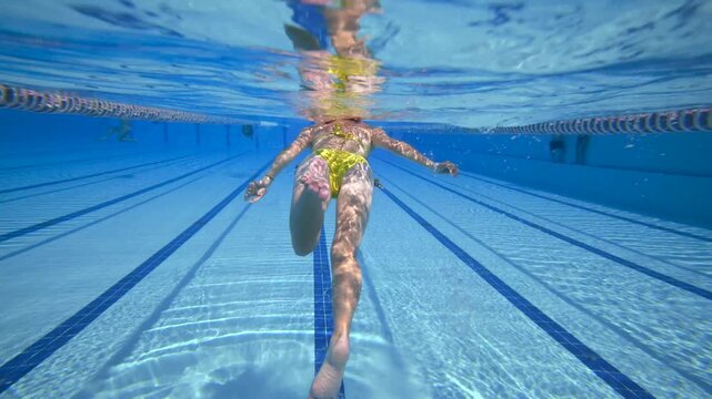 Underwater shot young woman swimming backstroke style in clear blue water swimming pool, healthy lifestyle and active sport workout activity.