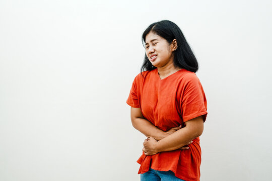 Sick Asian woman holding stomach suffering from severe abdominal pain or menstrual cramps isolated on white background