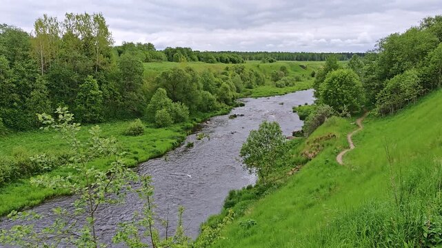Winding river through a green valley with a footpath along the bank, nature escape, exploration, eco tourism, mindful travel.