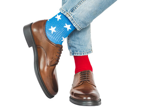 Men's legs, red and blue socks with white stars, paired with jeans and brown shoes. Bold fashion statement, creative individuality. Fun office fashion and personality at work concept. Studio shot