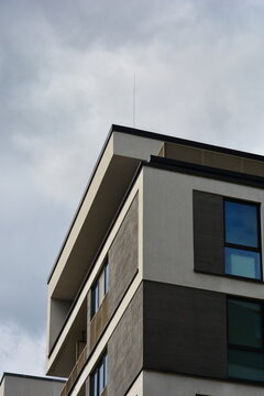 Fragment of the corner of a modern building with windows and a metal spire on the roof under gloomy clouds
