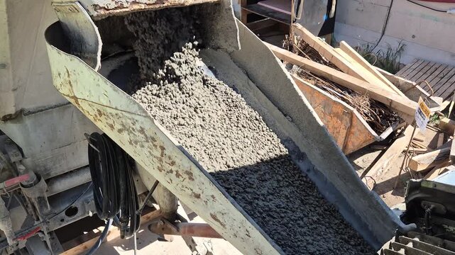 Fresh concrete flowing from the concrete mixer truck chute into the concrete pump hopper shot from a high side angle, normal speed footage