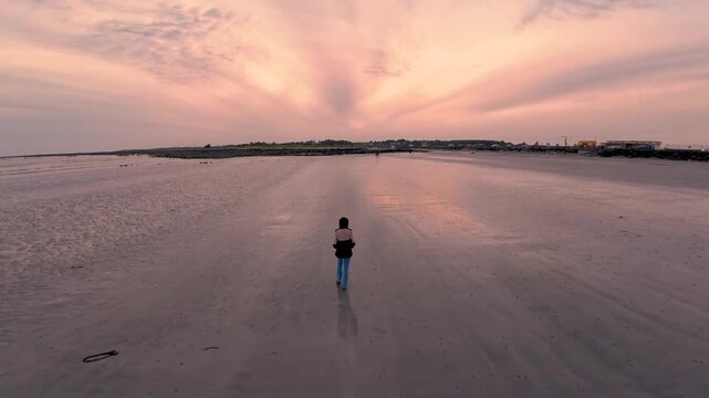 Sunset walk at Silverstrand Beach Galway with dramatic glowing sky, reflective shoreline and peaceful solitary woman enjoying Ireland&rsquo;s coastal beauty, wild Atlantic way