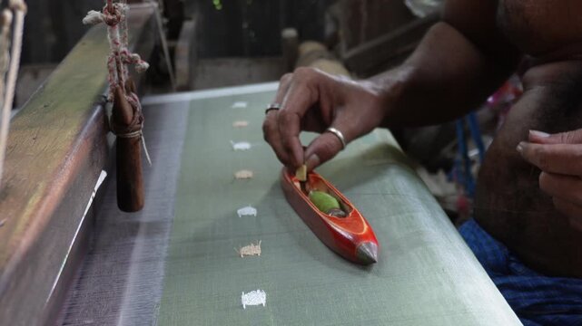 Artisan weaving fabric with wooden shuttle on handloom