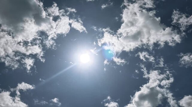 Bright sun shining through beautiful white clouds on blue sky.