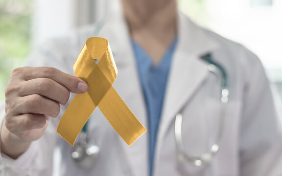 Childhood cancer awareness with gold ribbon on doctor's hand in medical background. Golden bow color for Embryonal Rhabdomyosarcoma, Neuroblastoma and Osteosarcoma awareness