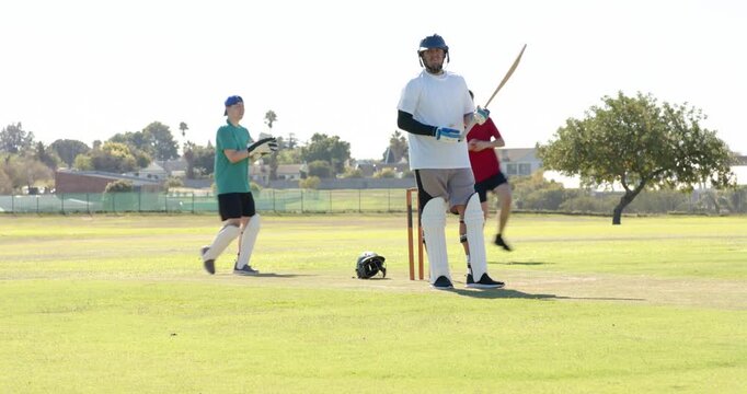 Cricketers bowling past stumps on field to test batsman, keeper returning ball, copy space