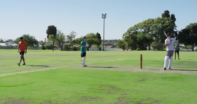 Bowler delivering male keeper in green on pitch catching breaking stumps, appealing dismissal