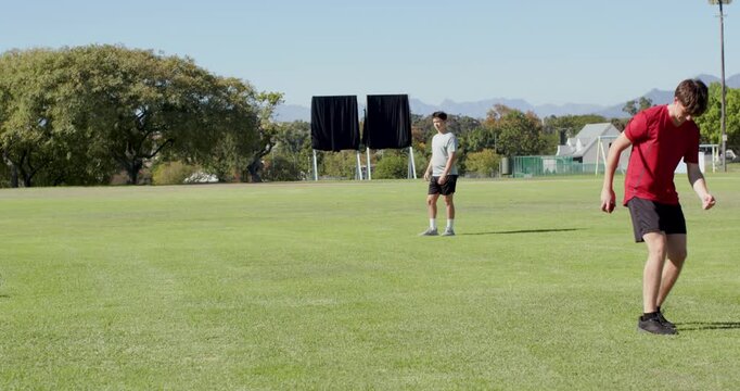 Teen bowler in red retrieving cricket ball on pitch, running to bowl over stumps, copy space