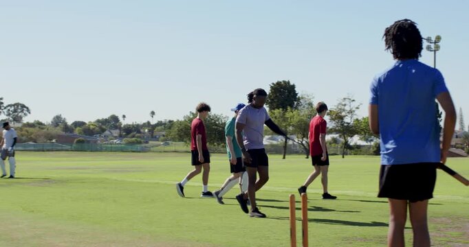 Diverse cricket team shaking hands with umpire after match, walking off pitch carrying stumps