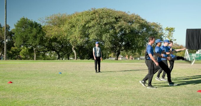 Guiding male trainees running knee drill on park field, with asian indian coach with red disk
