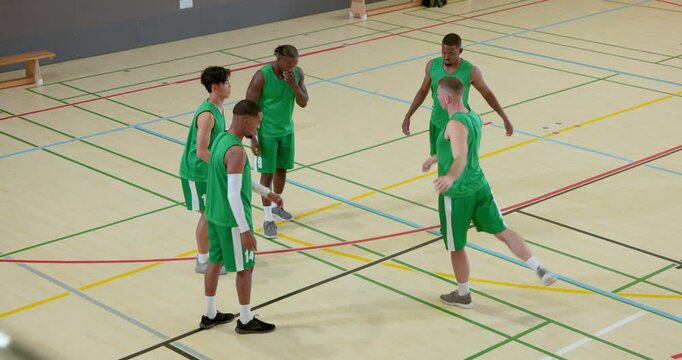 Starting drills with diverse male green-jerseyed team on court juggling basketball